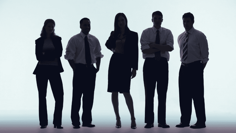 A group of 5 men and women stand in shadow